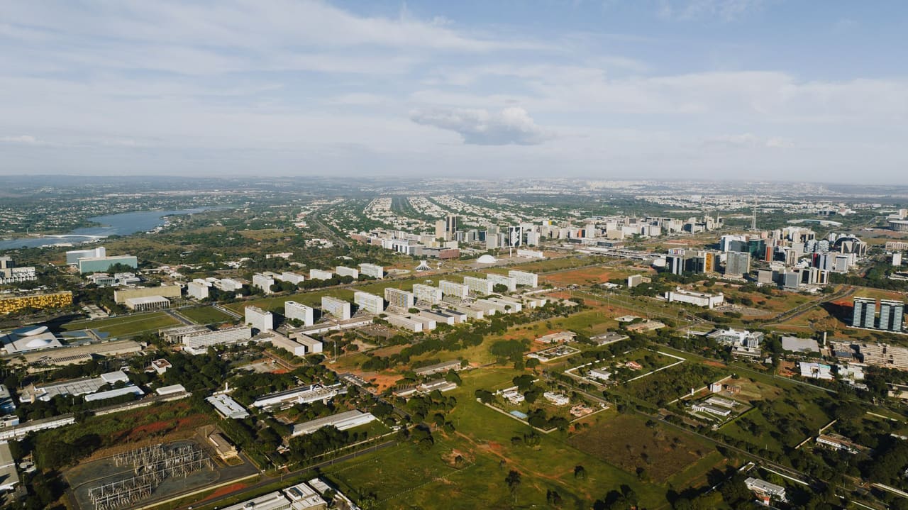Aerial shot of Brasília showcasing its urban landscape, buildings, and greenery in daylight.