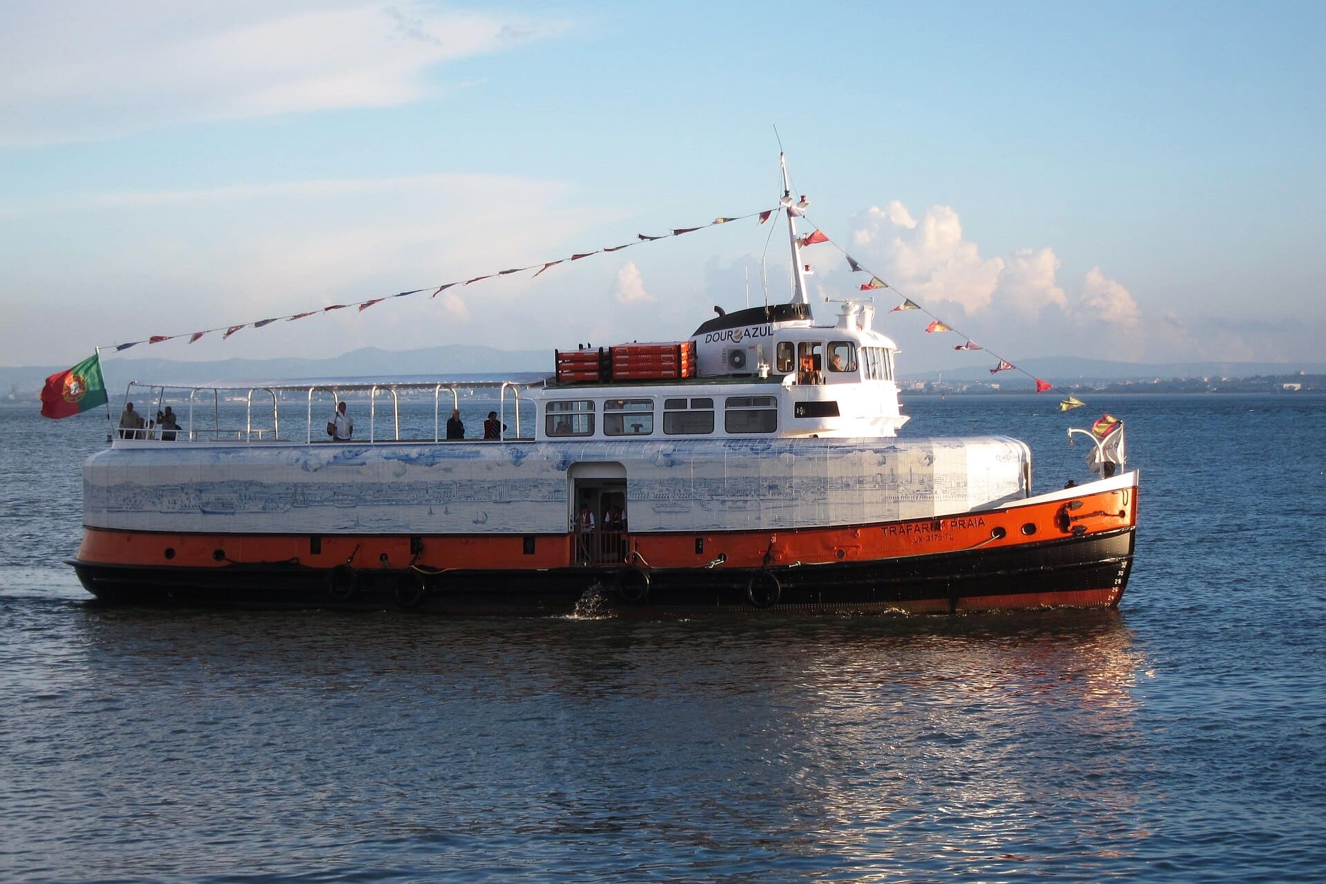 Trafaria Praia is a passenger ferry built in 1960 that used to ply the river Tagus between Lisbon and Cacilhas until it was decommissioned in 2011. Under the direction of Joana Vasconcelos, the ferry underwent a major transformation, which included encasing the exterior of the vessel from stern to prow in a wrap-around frieze of over 7,000 traditional tin-glazed, blue-and-white, hand-painted azulejo tiles depicting 20 kilometers, or 12 miles, of the Lisbon skyline, from the Bugio Tower to the Vasco da Gama Tower. Below the ship's deck, Joana Vasconcelos covered the ceiling and walls with blue and white fabrics and crocheted pieces intertwined with LEDS creating a mysterious, dark-blue sea cave that pulsates with fairy lights and gently vibrates with the ship's engine. It envelops visitors and elicits both an intellectual and a sensorial response. The ship was shown at the 55th Venice Biennale (2013) as the Portuguese pavilion; it currently moors not far from where actual passenger ferries carry commuters across the Tagus. It is open for visits and short river cruises.