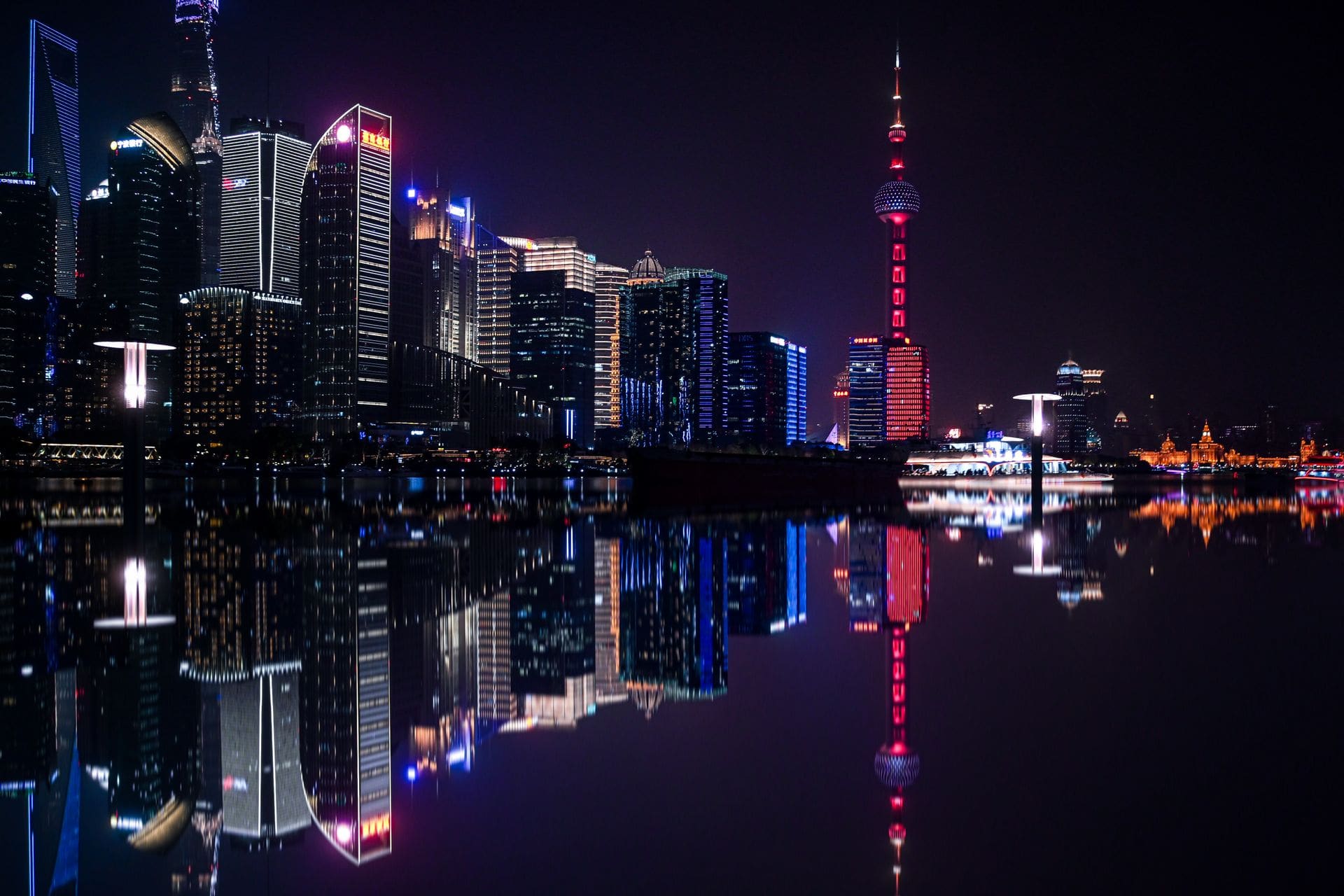 Dazzling night view of Shanghai's Pudong skyline with the iconic Oriental Pearl Tower reflecting on the water.