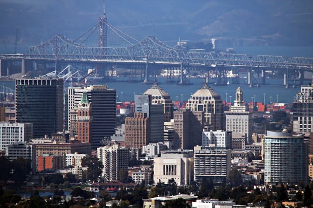 The Oakland skyline as seen from the Oakland hills. Oakland, CA has a population of about 400,000 and functions as the principal port city of Northern California. Both the old and new eastern span of the San Francisco-Oakland Bay Bridge can be seen in the background. It carries over 270,000 vehicles each day between the San Francisco Peninsula and the East Bay.