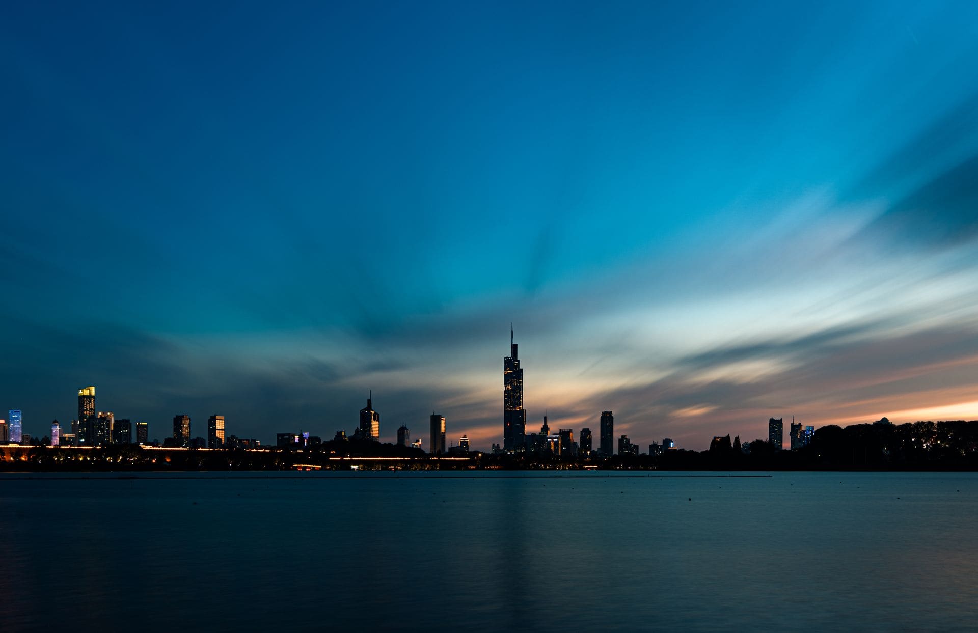 Beautiful city skyline view with dramatic twilight sky reflecting over calm waterfront, creating a serene urban landscape.