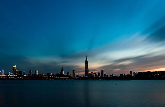 Beautiful city skyline view with dramatic twilight sky reflecting over calm waterfront, creating a serene urban landscape.