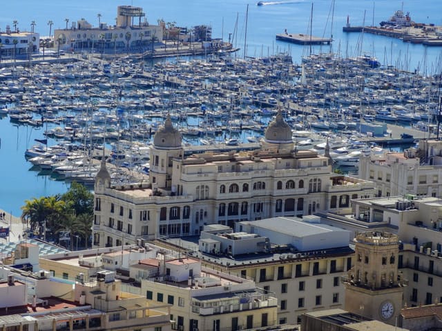 Aerial view of Alicante marina with boats and historic architecture under a clear blue sky.