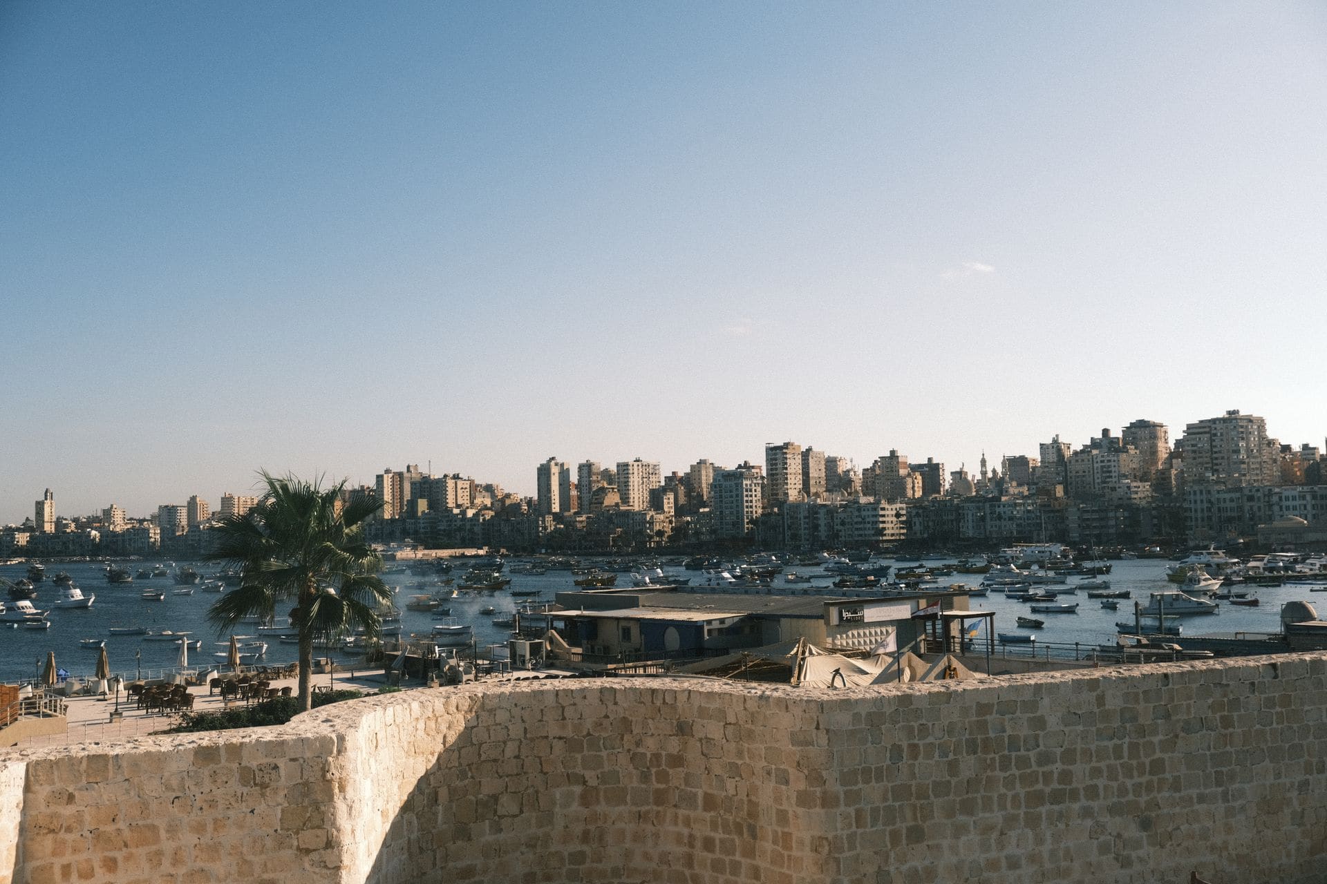 Captivating skyline of Alexandria with boats and historic fortifications against a clear sky.