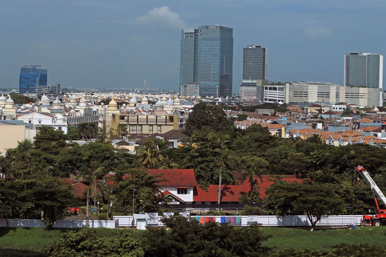 A vibrant cityscape featuring towering skyscrapers and lush greenery under a blue sky.