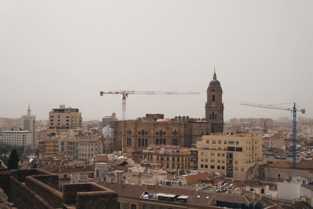 A stunning urban landscape featuring Malaga Cathedral amidst cranes and city buildings.