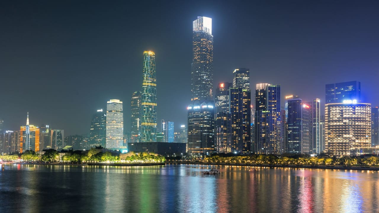 Illuminated skyscrapers of Guangzhou reflecting on the water under a night sky.