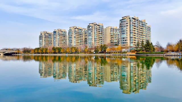 High-rise apartments reflect on a tranquil waterfront in Zhengzhou, China, showcasing urban architecture.