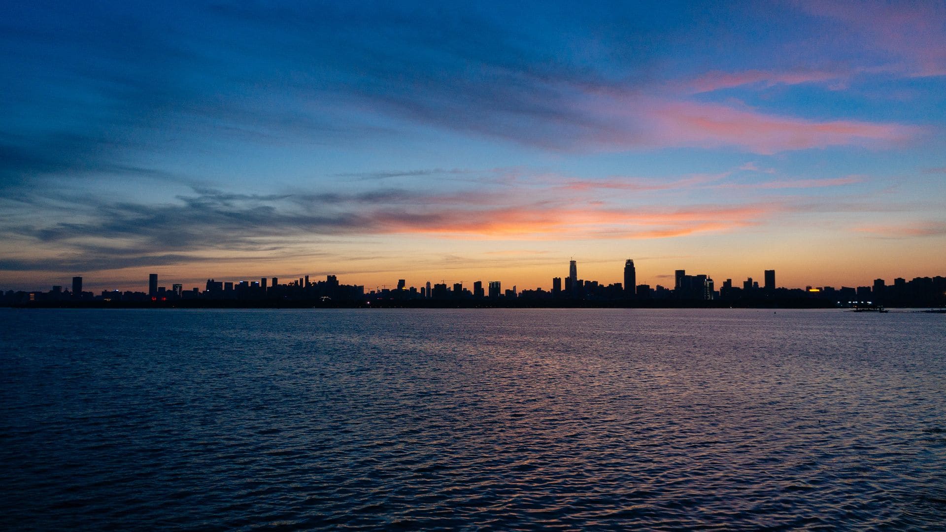 The serene skyline of Wuhan silhouetted against a twilight sky over a calm river.