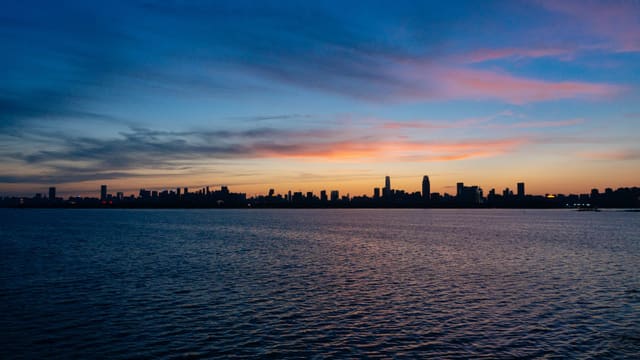 The serene skyline of Wuhan silhouetted against a twilight sky over a calm river.