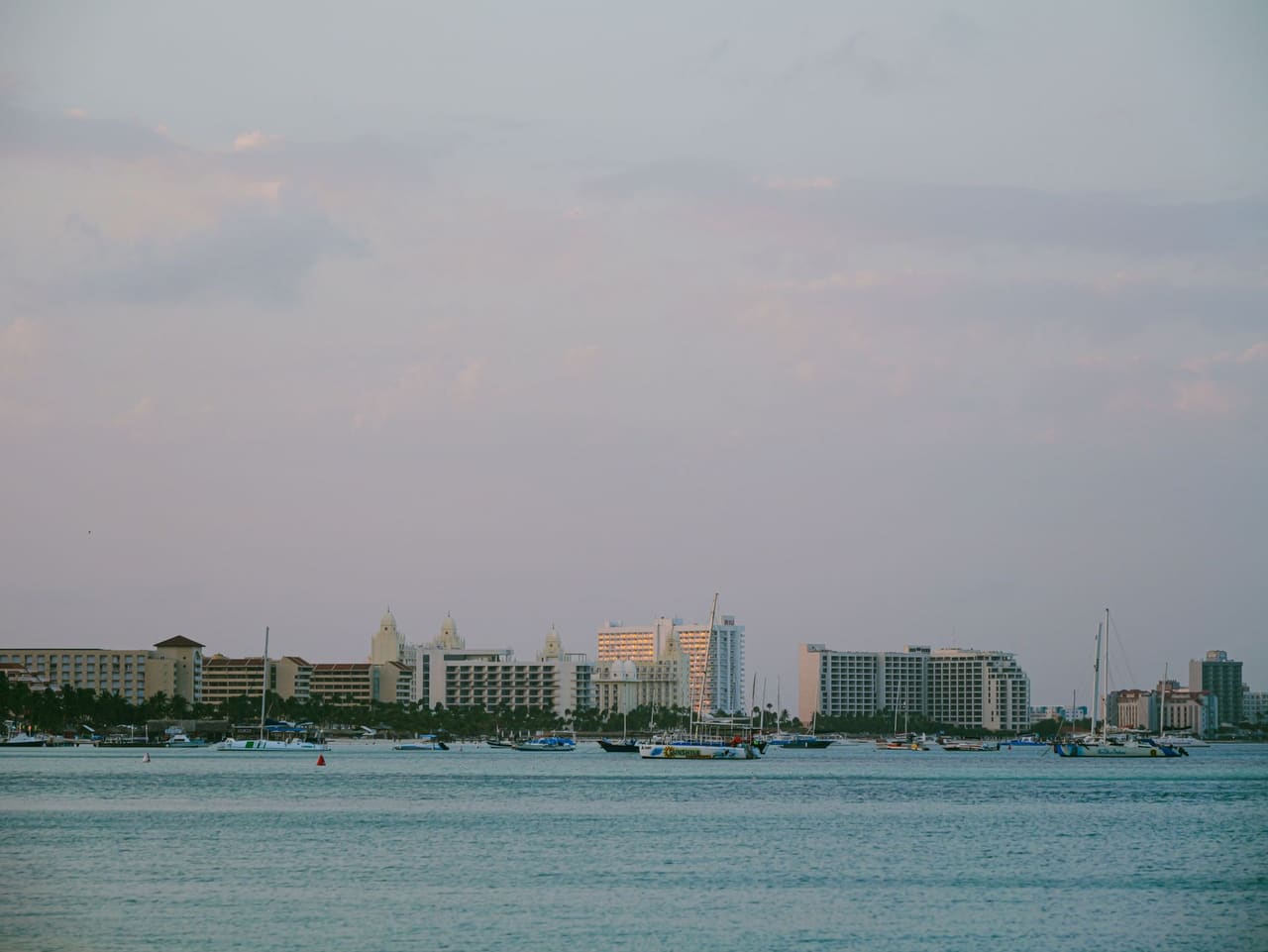 A serene view of a coastal cityscape with boats and buildings at twilight, under a pastel sky.