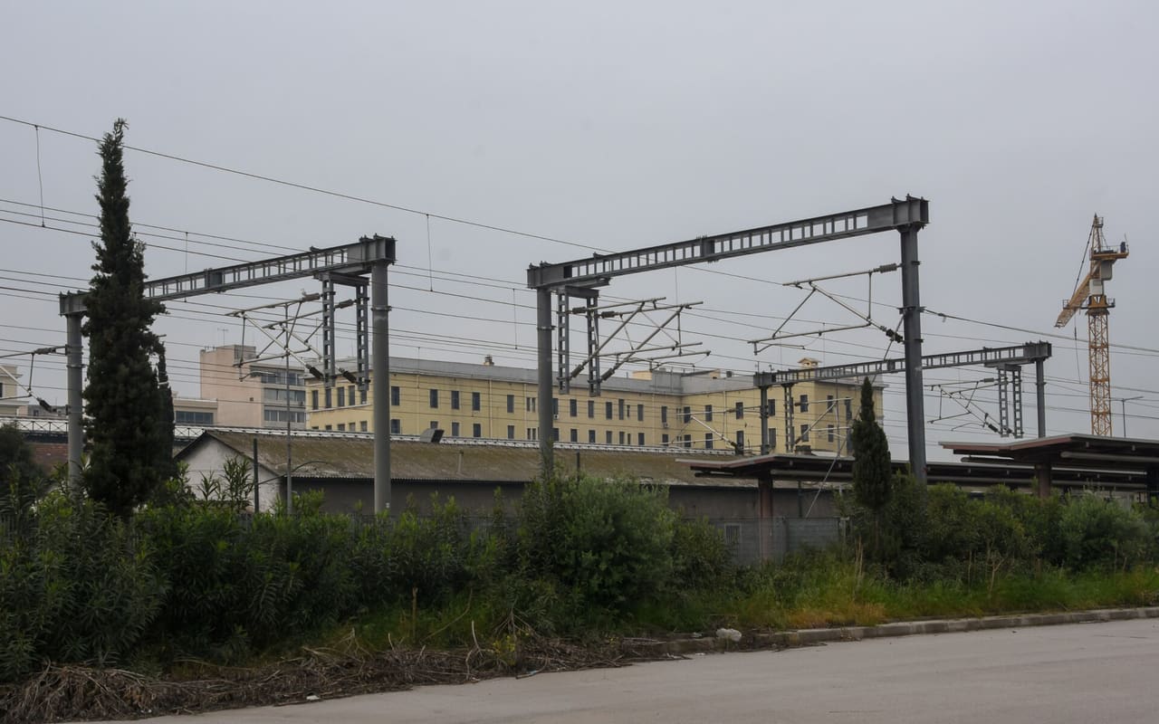 500px provided description: Just before approaching the terminal station of the suburban railway. In the background, the yellow building is the metro line 1 building and station. [#sky ,#train ,#cityscape ,#building ,#plant ,#railway station ,#metro station ,#Aghia Sophia ,#suburban railway ,#Pireas ,#electricity wire