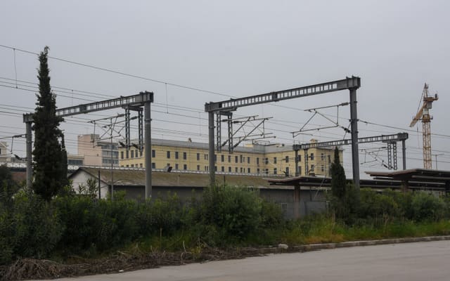 500px provided description: Just before approaching the terminal station of the suburban railway. In the background, the yellow building is the metro line 1 building and station. [#sky ,#train ,#cityscape ,#building ,#plant ,#railway station ,#metro station ,#Aghia Sophia ,#suburban railway ,#Pireas ,#electricity wire