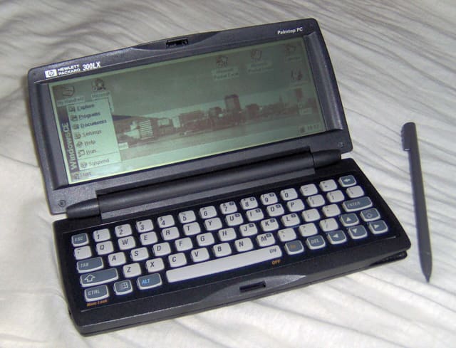The HP 300LX hpc with stylus, showing Windows CE 1.0. The wallpaper shows the skyline of the Norwegian city of Bergen.